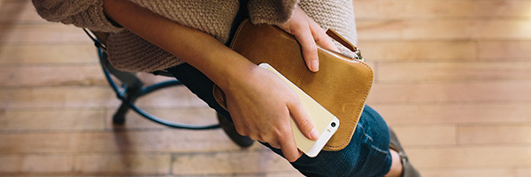 Woman sitting on a stool holding a leather notebook and a smartphone