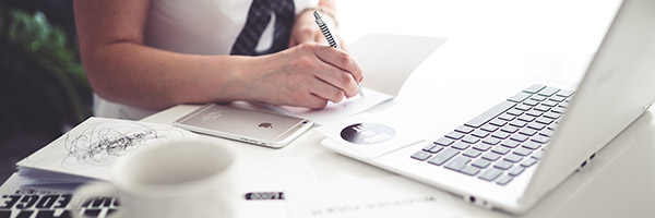 Photo of a woman sitting at a desk while writing on a notepad