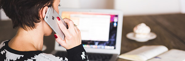 Photo of a person holding a mobile phone to their ear while working on a laptop