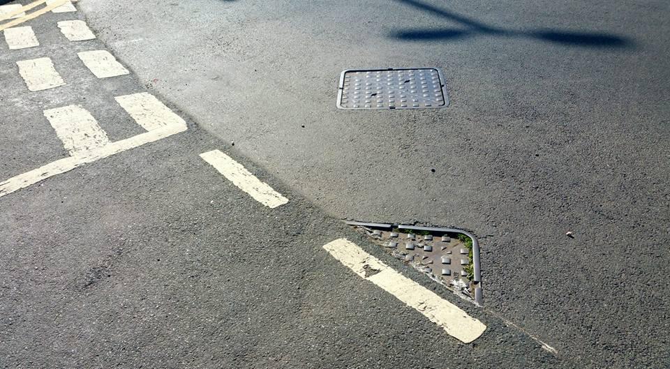 A service hatch on a road which has been partly tarmacked over in error