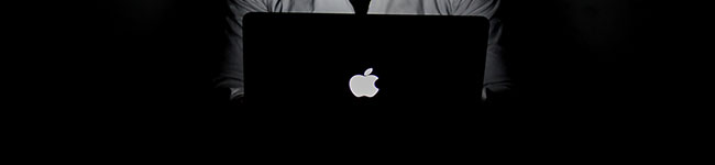 A person using a Macbook illuminated only by the screen